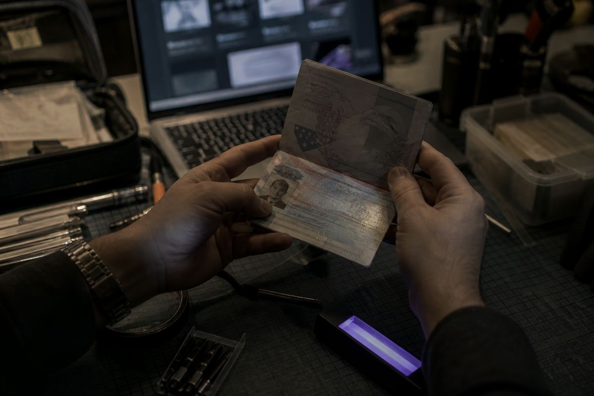 A person inspecting a counterfeit US passport on a cluttered table, highlighting illegal passport acquisition.